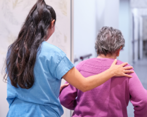 Nursing home staff walking with an elderly patient, seen from behind.