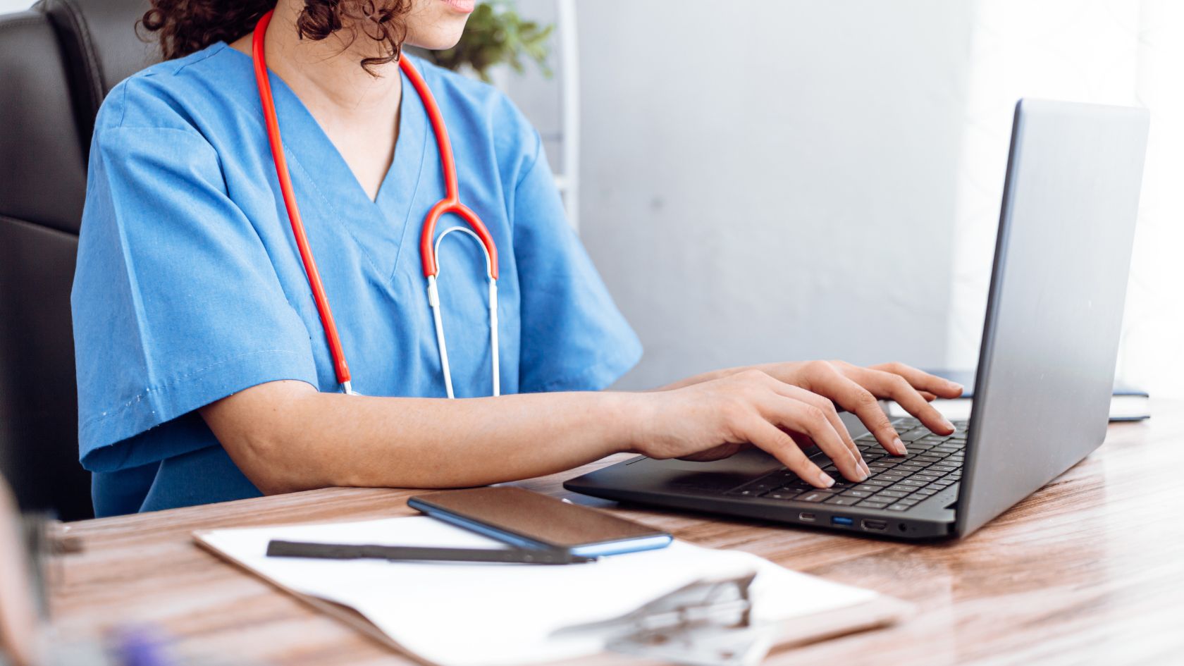 nurse sitting at desk, working on a laptop.